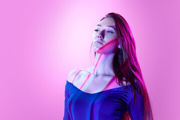 Beautiful, tender young woman posing against light purple background in neon lights with neon...