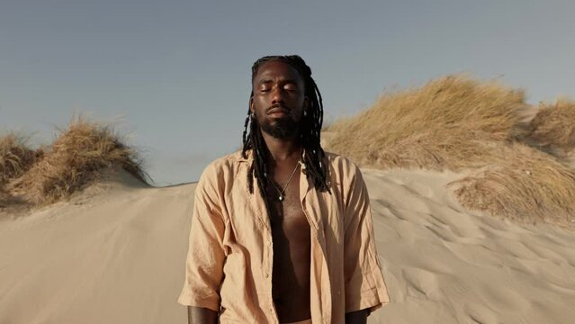 A stylish black male stands in deep meditation, eyes closed, breathing on a sandy desert, symbolizing a profound connection with inner self