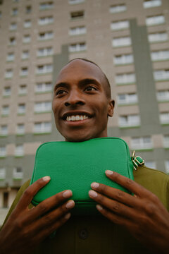 Closeup portrait of young man with autism in street wear and green purse smiling in urban area