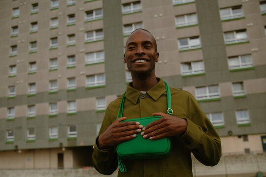 Analogue style portrait of young man with autism in street wear holding green purse and smiling