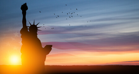 Statue of Liberty with american flag and flying birds on background of sunset sky. Close-up....