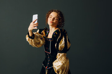 Portrait of a young aristocratic woman holding mobile phone dressed in a medieval dress doing...