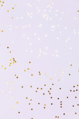 Gold sparkle confetti stars on a lavender pastel background. Glitter, shine, bright. Christmas festive flat lay, winter holiday, new year, happy birthday concept. Flat lay, top view, copy space.