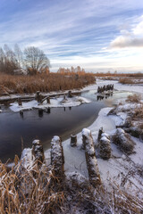 Wooden piles from an old destroyed bridge over the river. Winter landscape with frozen river and blue sky with clouds, nature series