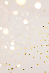 Festive gold background. Shining stars confetti and fairy lights on beige background. Christmas....