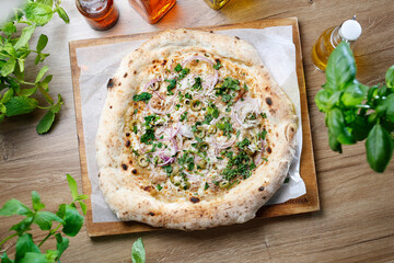 Freshly baked pizza with cheese, onion, olives, fresh herbs, on a wooden cutting board, top view, selective focus.