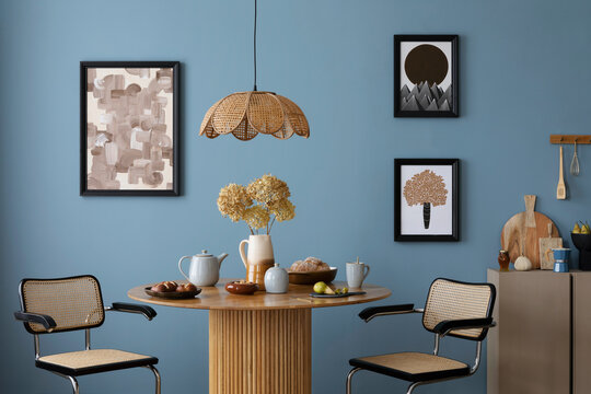 Interior design of cozy dinning room and kitchen interior with mock up poster frame, round table, rattan armchair, beige sideboard, vase with flowers and personal accessories. Home decor. Template.