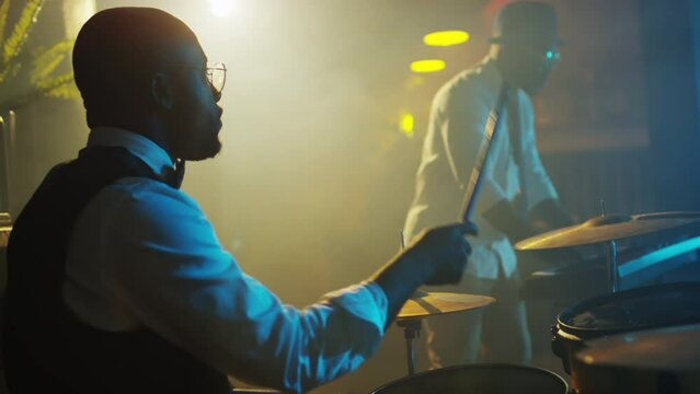 Medium slowmo of Black male jazz musician in elegant outfit playing drums during live concert in stage in club at night