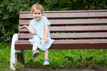 Satisfied girl sitting on the edge of a long wooden bench in the park