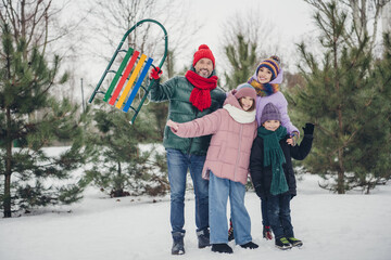 Photo of positive excited husband wife small kid wear windbreaker cuddling together rising sleigh outside urban city park