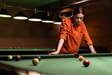 Woman in shirt with cue pointing at billiard ball at table. Playing billiards concept
