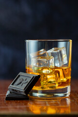 A glass of whiskey and ice, chocolate stands on an old polished table ion dark background