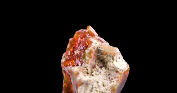 fire opal crystal 360° rotation in 4k isolated on black background. macro detail close-up rough raw unpolished semi-precious gemstone.