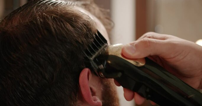 Handsome man getting new hairstyle with electric trimmer. Close Up with trimmer work. Young hipster Caucasian man during beard and mustache grooming in modern barber shop. Men's hair styling. 
