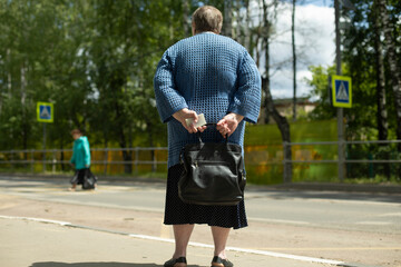 Pensioner is waiting for bus on road. Grandma with bag. Elderly woman in city.