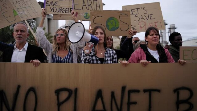 Group of people from different ages and nationalities gathered to protest against factories and pollution. Manifestation in favor of the earth with banners for Climate change.