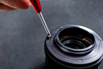Opening a vintage camera lens, screw driver and tiny screws, selective focus close up