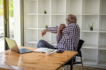 Senior black man stretching his muscles while working on a laptop computer.