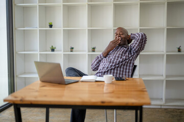 Senior black man yawning and stretching lazy while working with a laptop computer.