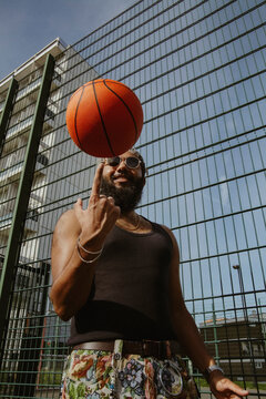 Young Tamil man in cool outfit spinning basketball on finger in front of court