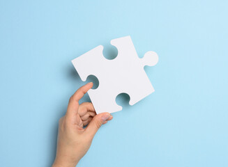 A female hand holds a white paper puzzle piece against a blue background
