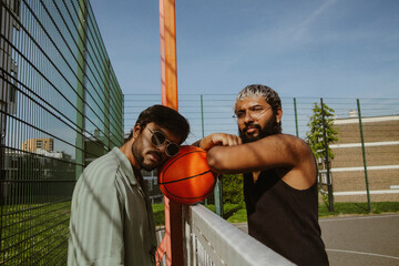 Obraz premium Portrait of two young multiracial friends in trendy clothes posing with basketball on court