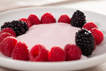 Fresh raspberries and blackberries laid out on a white plate in circle with yogurt