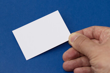 Hand of man holding paper card isolated on blue background, business card showing.