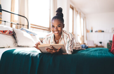 Happy black woman with book on comfortable bed