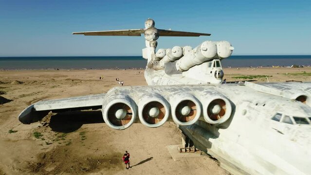 a white ekranoplane is standing on the seashore, on a sandy beach, tourists are walking around, a drone shot, slow motion, flying around the plane, airplane details