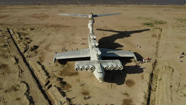 an abandoned white ekranoplane stands on a sandy beach, against the background of the sea, tourists walk around. , slow motion, drone shot, smooth camera movement, wide view, the plane is completely