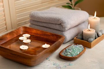Beauty spa treatment items on white wooden table. Candles, stones, sea salt and towels. Cosy bath.
