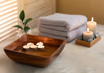 Beauty spa treatment items on white wooden table. Candles, stones, bowl with water and towels. Cosy bath.