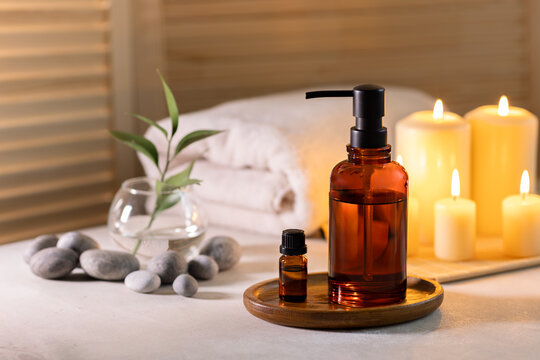 Beauty spa treatment items on white wooden table. Candles, stones, essential oils and towels. Cosy bath.