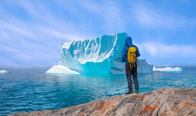 Environmental Concept - A Man Hiker looking at melting Ginat  glacier - Melting of a iceberg and pouring water into the sea - Greenland - Tiniteqilaaq, Sermilik Fjord, East Greenland
