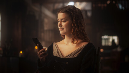 Innovation Concept: Beautiful Female in Medieval Clothes Using Smartphone Indoors. Princess in her Castle Texting Friends, Posting on Social Media, Looking for her Prince Charming on Dating Apps