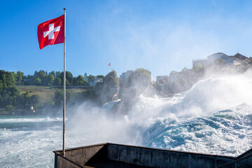 Switzerland travel - Flag of Switzerland flying over the Rhine Falls in Laufen-Uhwiessen
