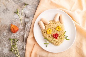 Funny quinoa porridge, and small sausages in form of cat face on brown concrete. top view.