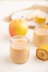 Baby puree with fruits mix, apple, banana infant formula in glass jar on white, side view, selective focus