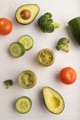 Baby puree with vegetable mix, broccoli, avocado in glass jar on white wooden, top view