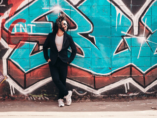 Handsome hipster model. Arabian man dressed in suit jacket clothes. Fashion male with long curly hairstyle posing in street near graffiti wall