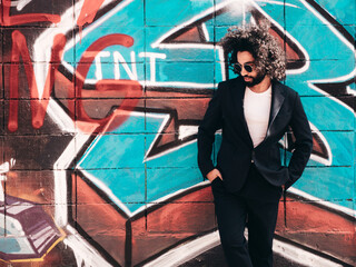 Handsome hipster model. Arabian man dressed in suit jacket clothes. Fashion male with long curly hairstyle posing in street near graffiti wall