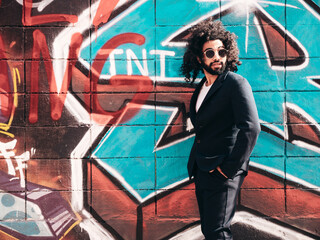Handsome hipster model. Arabian man dressed in suit jacket clothes. Fashion male with long curly hairstyle posing in street near graffiti wall