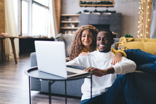 Relaxed African-American couple in living room, woman and man browsing website on laptop computer while shopping
