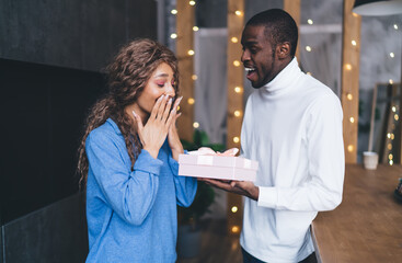 Astonished Caucasian woman receiving a pink gift box from a gleeful Black man