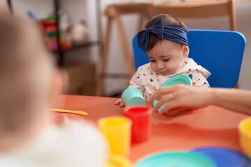 Adorable toddler playing with dish toy sitting on table at kindergarten