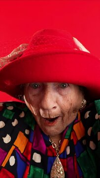 Vertical video of funny fisheye portrait of elderly senior old woman with wrinkled skin looks at camera gives great idea gesture showing explosion of thinking posing isolated on red background.