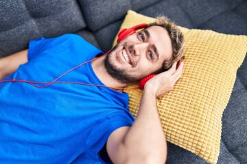 Fototapeta premium Young man listening to music lying on sofa at home