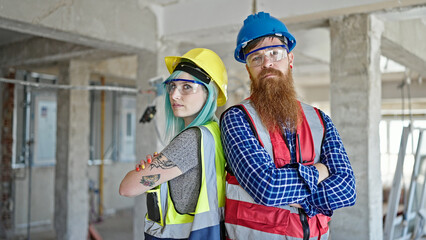 Man and woman builders standing with arms crossed gesture and relaxed expression at construction...