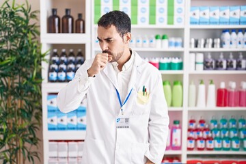 Handsome hispanic man working at pharmacy drugstore feeling unwell and coughing as symptom for cold or bronchitis. health care concept.